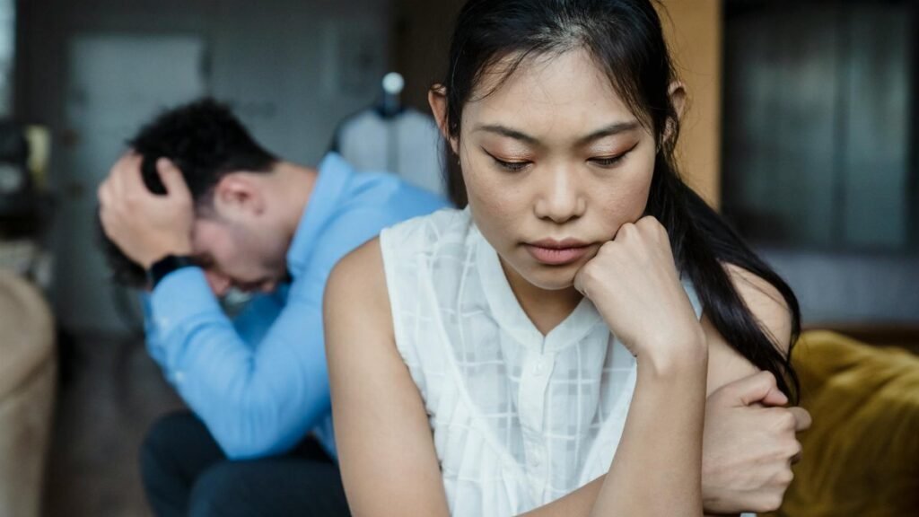 A couple experiencing relationship tension sitting silently on a sofa.