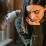 Crop woman tapping shoulder and comforting upset female friend while sitting at home together