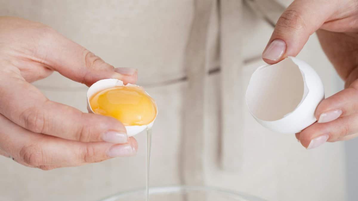 Detailed image of hands carefully cracking an egg into a bowl, showcasing cooking preparation.