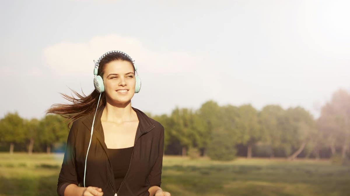 Smiling woman jogging in a park, listening to music with headphones, and enjoying the sunny day.