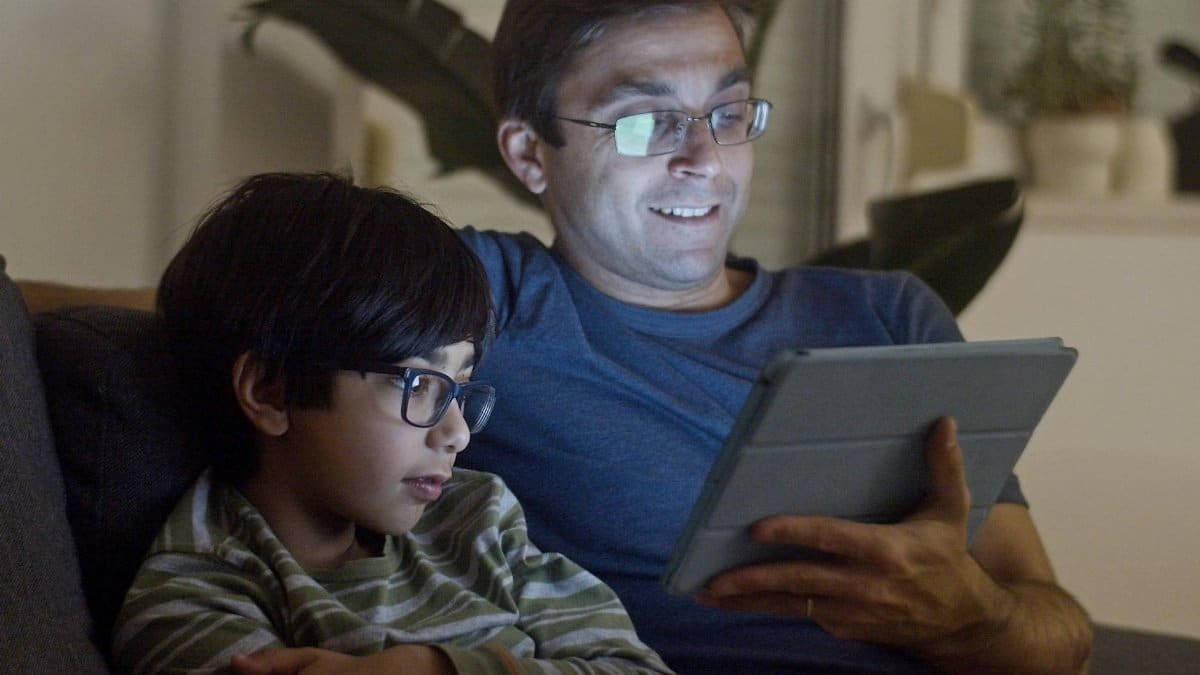 A father and son enjoy quality time using a tablet together indoors, creating a warm and intimate moment.