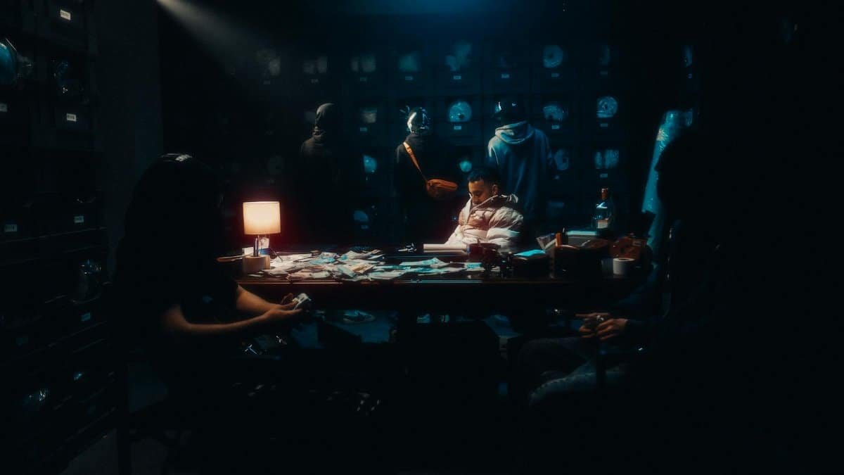 Atmospheric photo of a dimly lit club with masked figures around a table, evoking mystery.