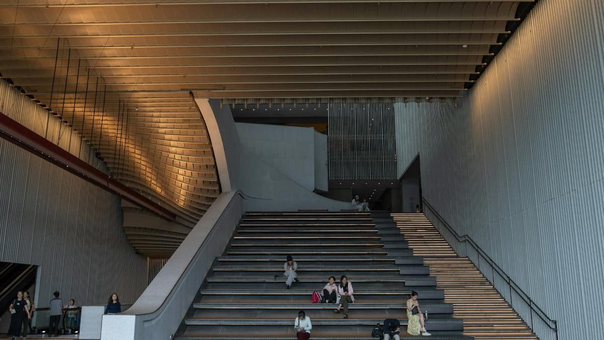 A contemporary interior staircase with ambient lighting and people sitting on the steps, showcasing modern architecture.