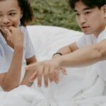 A young couple relaxes outdoors on white bed linen, enjoying a peaceful morning together.