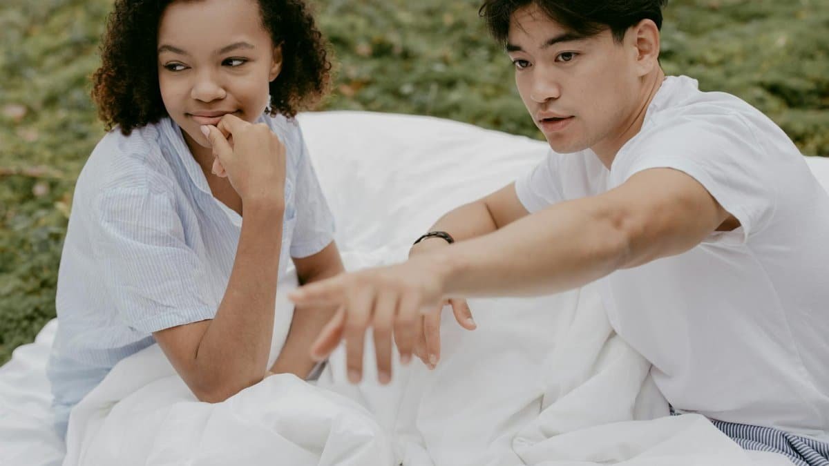 A young couple relaxes outdoors on white bed linen, enjoying a peaceful morning together.