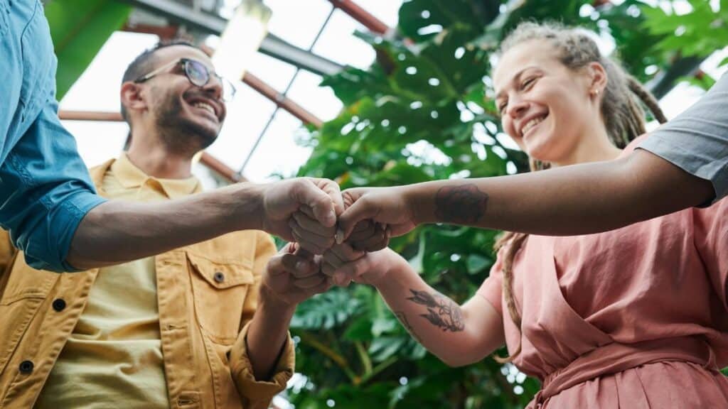 A group of young adults celebrating teamwork with a fist bump in a lush outdoor setting.