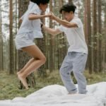 A joyful couple jumping on a bed outdoors in a peaceful forest setting.