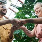 A group of young adults celebrating teamwork with a fist bump in a lush outdoor setting.