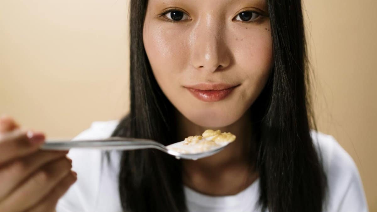 Portrait of an Asian woman holding a spoonful of cereal indoors, capturing a candid breakfast moment.
