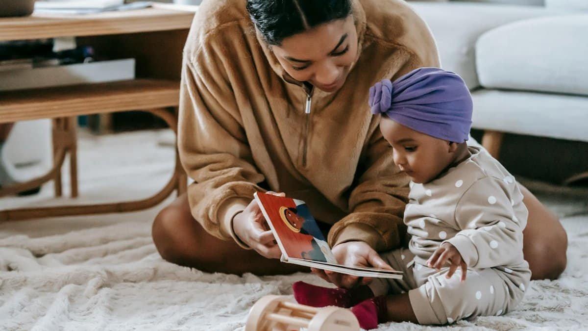 A mother and her baby bonding over a book on the floor of a cozy living room.
