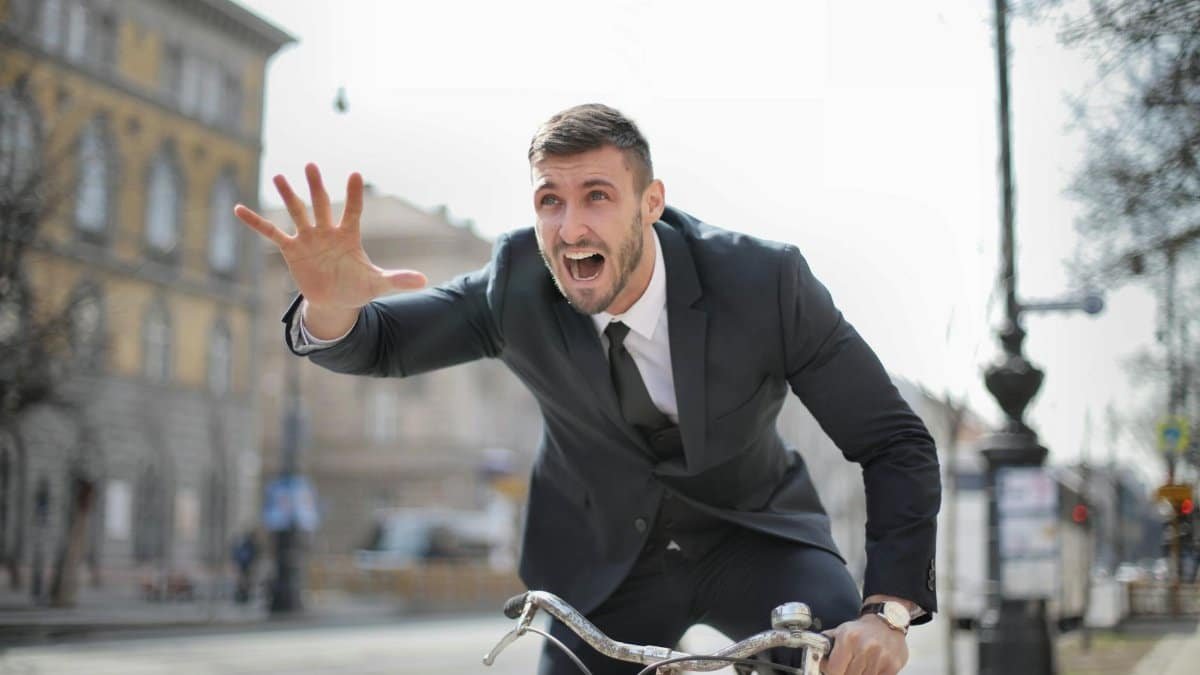 Corporate professional in a suit rides a bike swiftly through city streets expressing urgency.