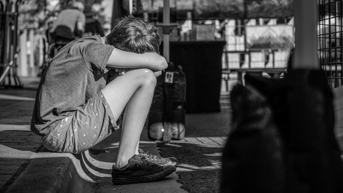A child sitting alone on a curb, depicting solitude and contemplation in a monochrome city setting.