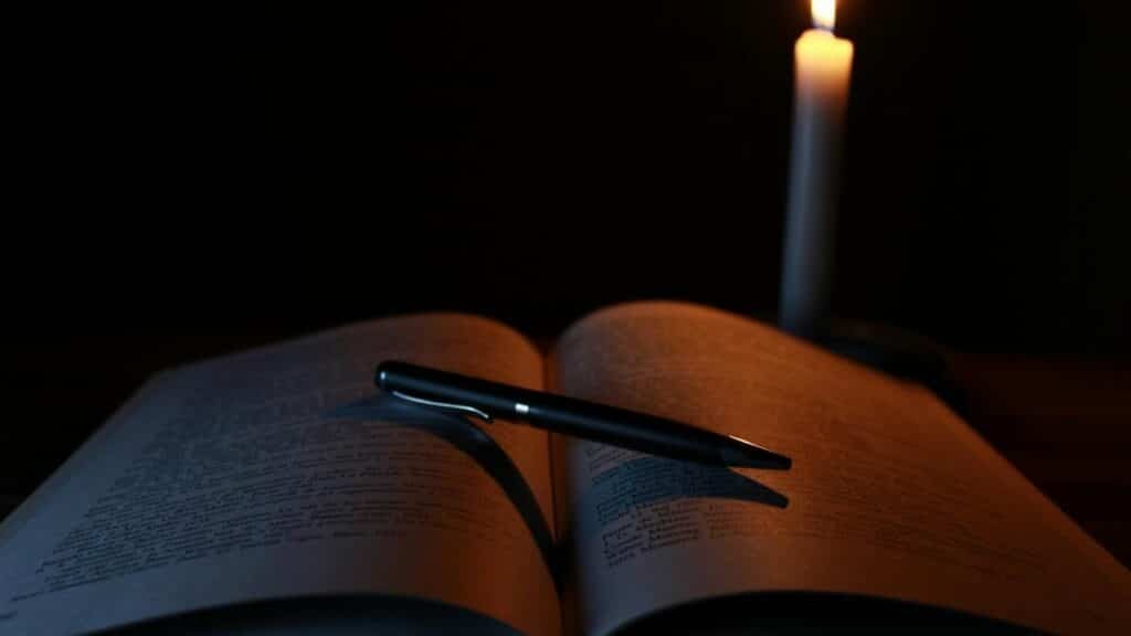 An open book and pen on a desk illuminated by candlelight, creating a tranquil study atmosphere.