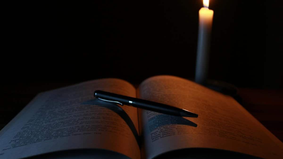 An open book and pen on a desk illuminated by candlelight, creating a tranquil study atmosphere.