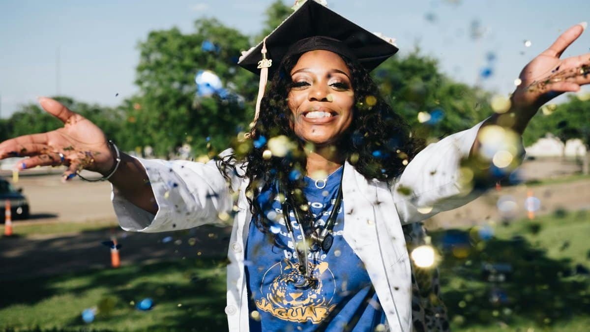 African American woman celebrating graduation with confetti outdoors, filled with happiness and success.