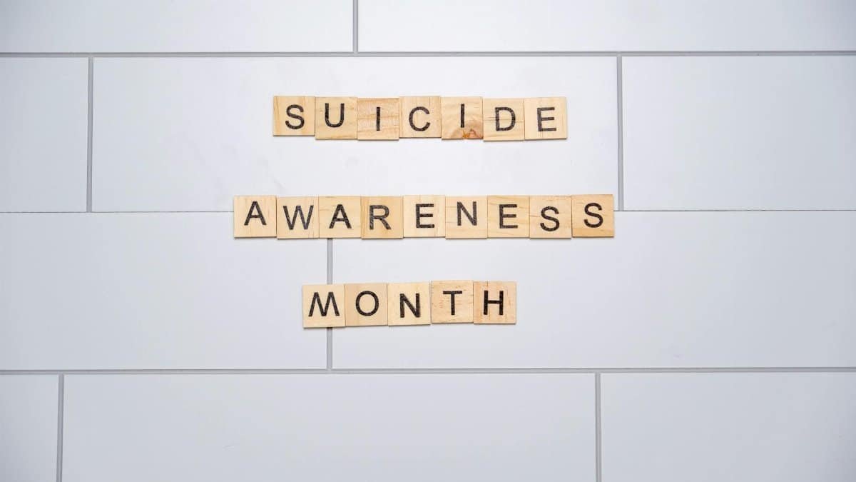 Wooden tiles spelling 'Suicide Awareness Month' on a white tiled background.