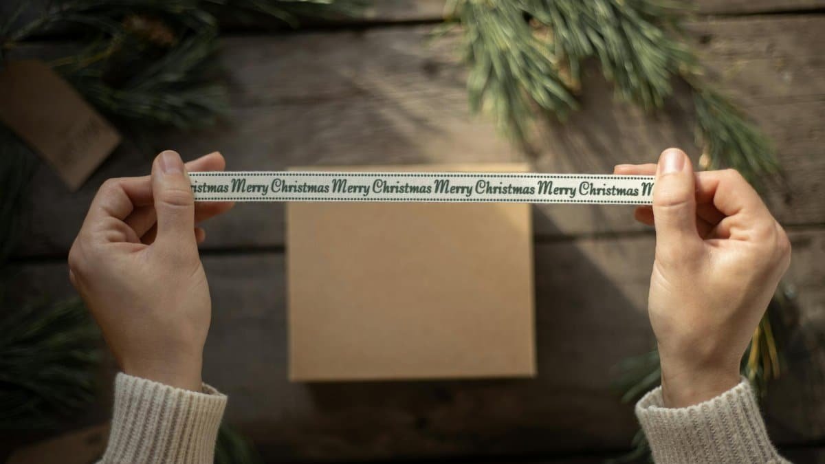 Unrecognizable male holding ribbon with sign Merry Christmas on timber background with spruce branches