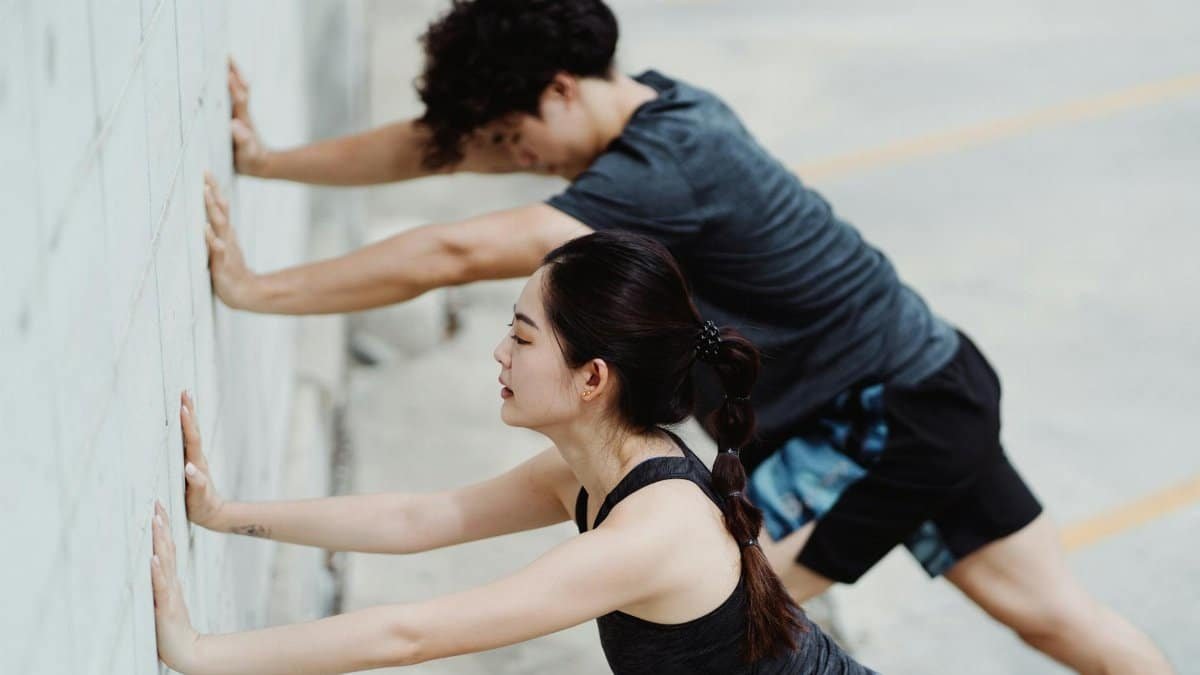 Two adults exercising and stretching against an outdoor urban wall, focusing on fitness and well-being.