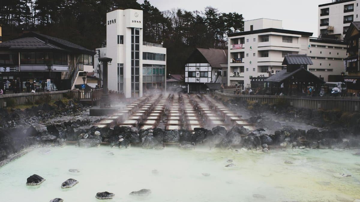 A tranquil hot spring town with steam rising from mineral-rich waters, surrounded by traditional architecture.