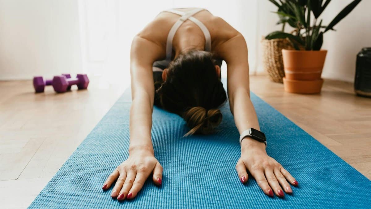 Woman doing a child's pose on a blue yoga mat at home, promoting fitness and wellbeing.