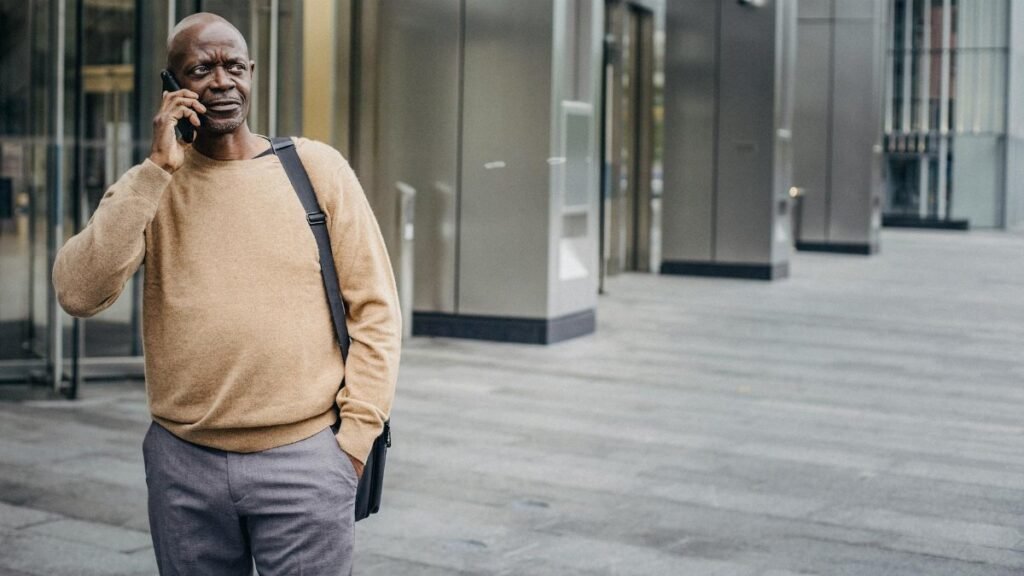 Focused African American man with hand in pocket chatting on mobile phone standing in downtown center