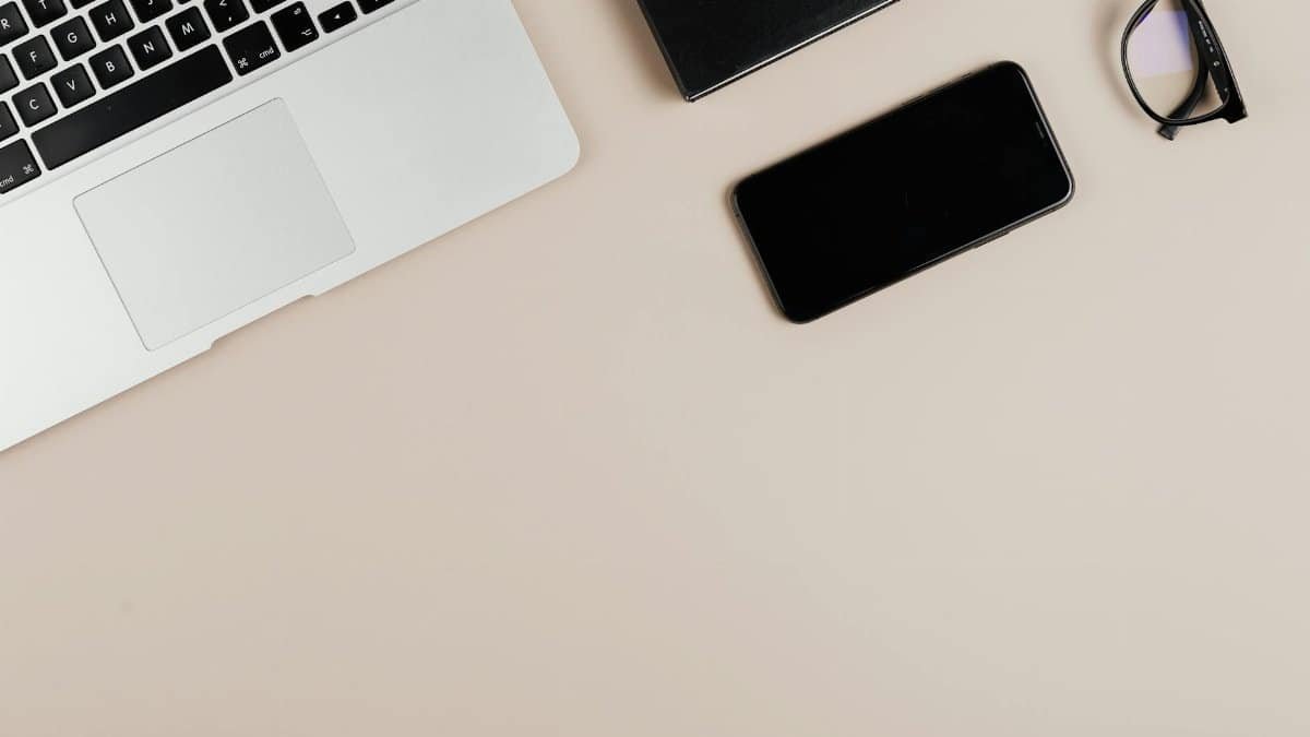 Modern workspace with laptop, smartphone, and eyeglasses on a beige surface. Ideal for tech or productivity themes.