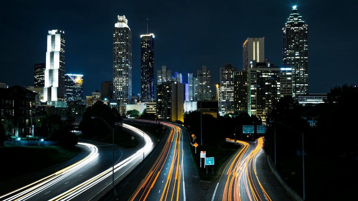 A vibrant cityscape at night showcasing light trails on the highway beneath towering skyscrapers.
