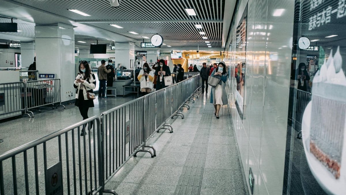 People wearing masks walk through an urban subway station with steel railings, showcasing city life.
