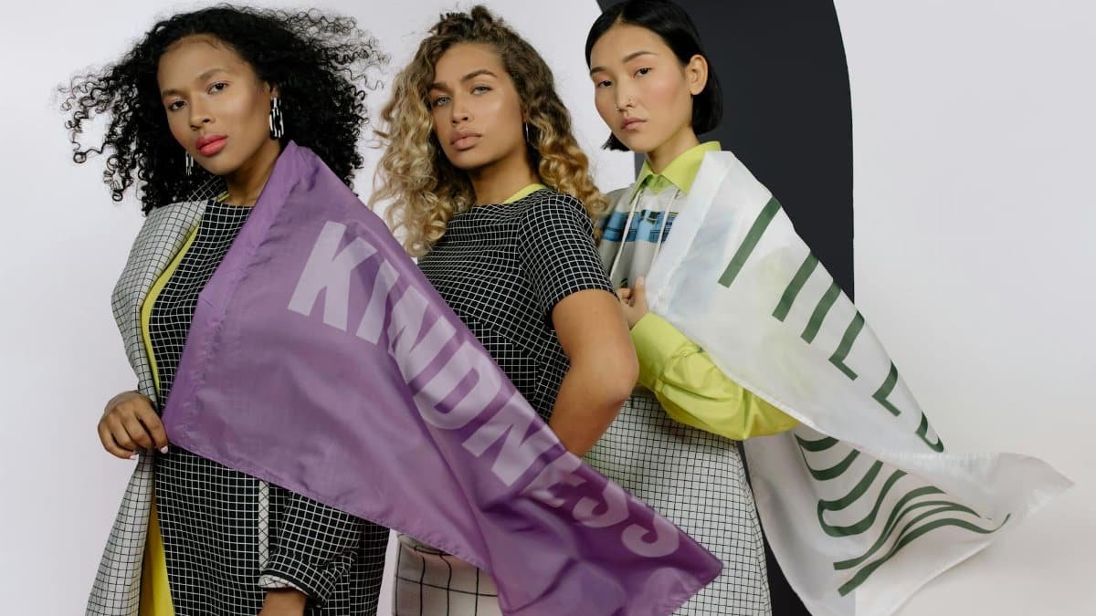 Three women holding flags with messages of kindness and wellness, highlighting unity and diversity.