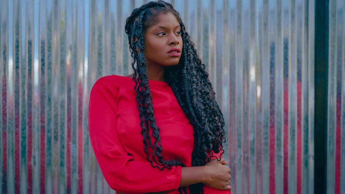 A woman in a vibrant red dress poses thoughtfully outdoors, reflecting style and elegance.
