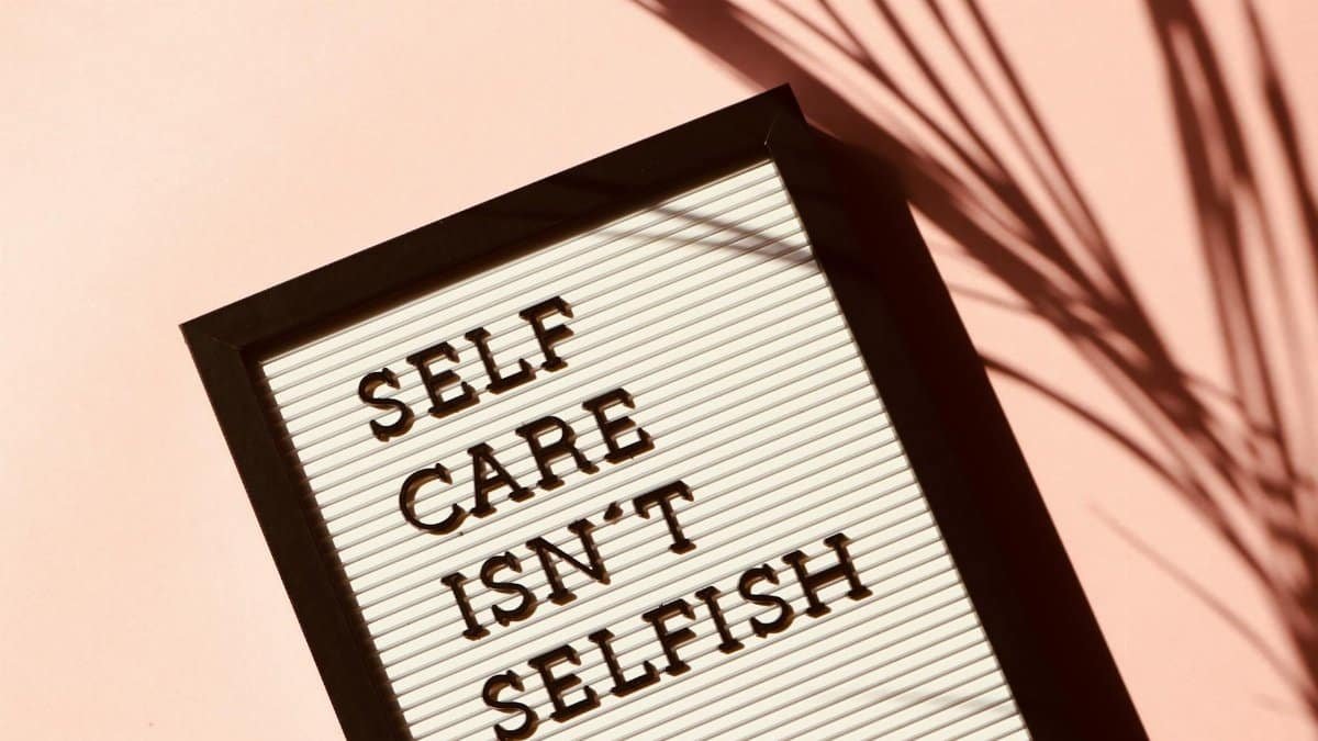 Letter board displaying 'Self Care Isn't Selfish' with artistic shadow on pink background.
