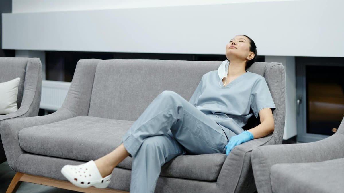 Nurse in scrubs takes a break, resting on a comfy hospital couch after a long shift.