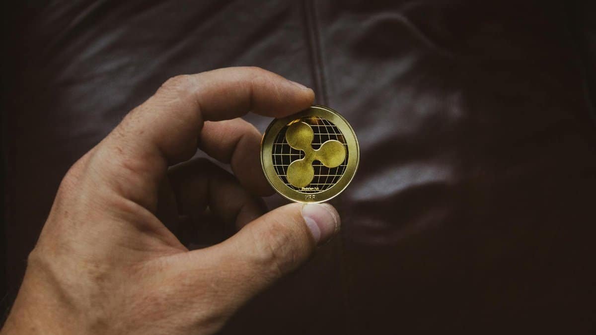 A close-up of a hand holding a gold Ripple cryptocurrency coin, symbolizing digital currency concept.