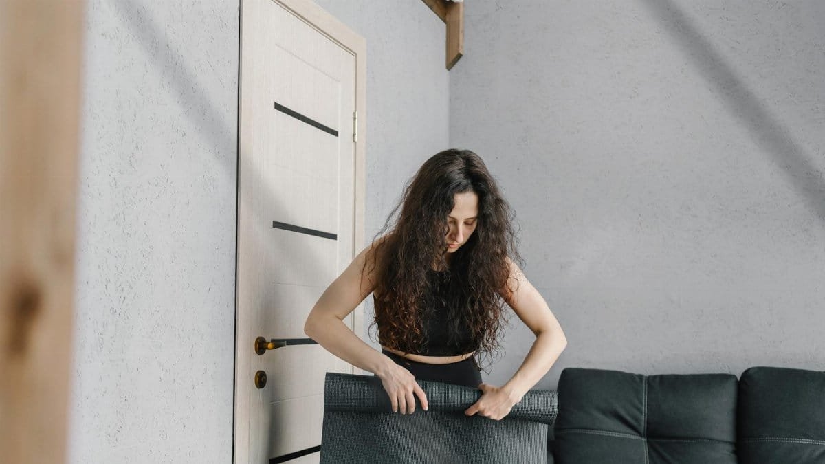 A woman sets up an exercise mat in a modern, minimalist apartment living room.