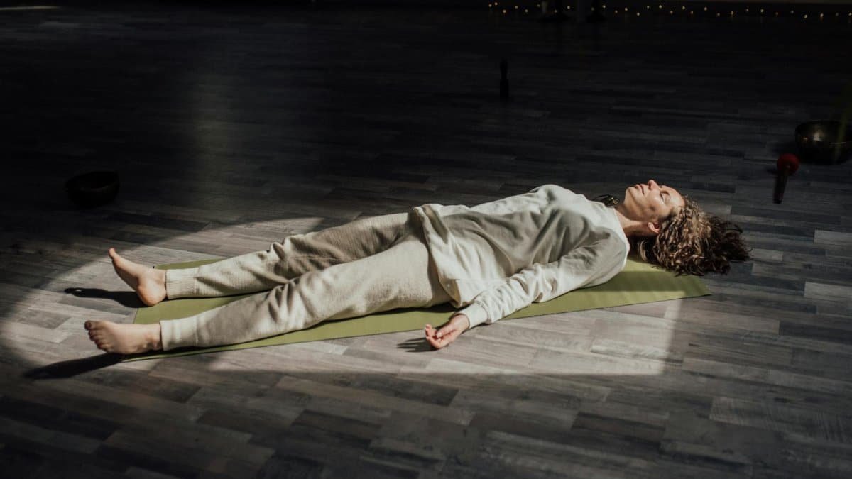 Woman lying on a yoga mat indoors, meditating and relaxing in a calm setting.