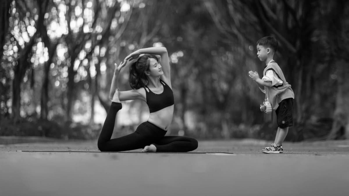 Black and white photo of a woman practicing yoga with a child in a peaceful outdoor setting.