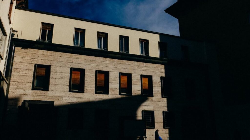 Silhouette of a person walking by a sunlit building, creating dramatic shadows.