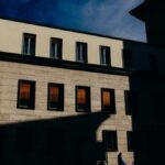 Silhouette of a person walking by a sunlit building, creating dramatic shadows.