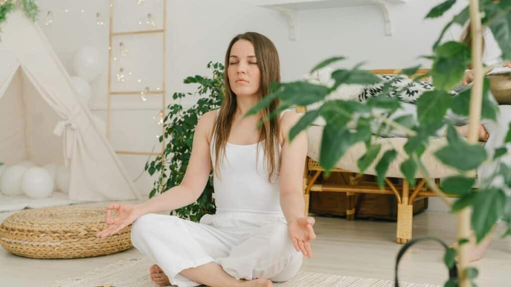 Peaceful meditation scene with a woman practicing mindfulness in a cozy, plant-filled indoor space.