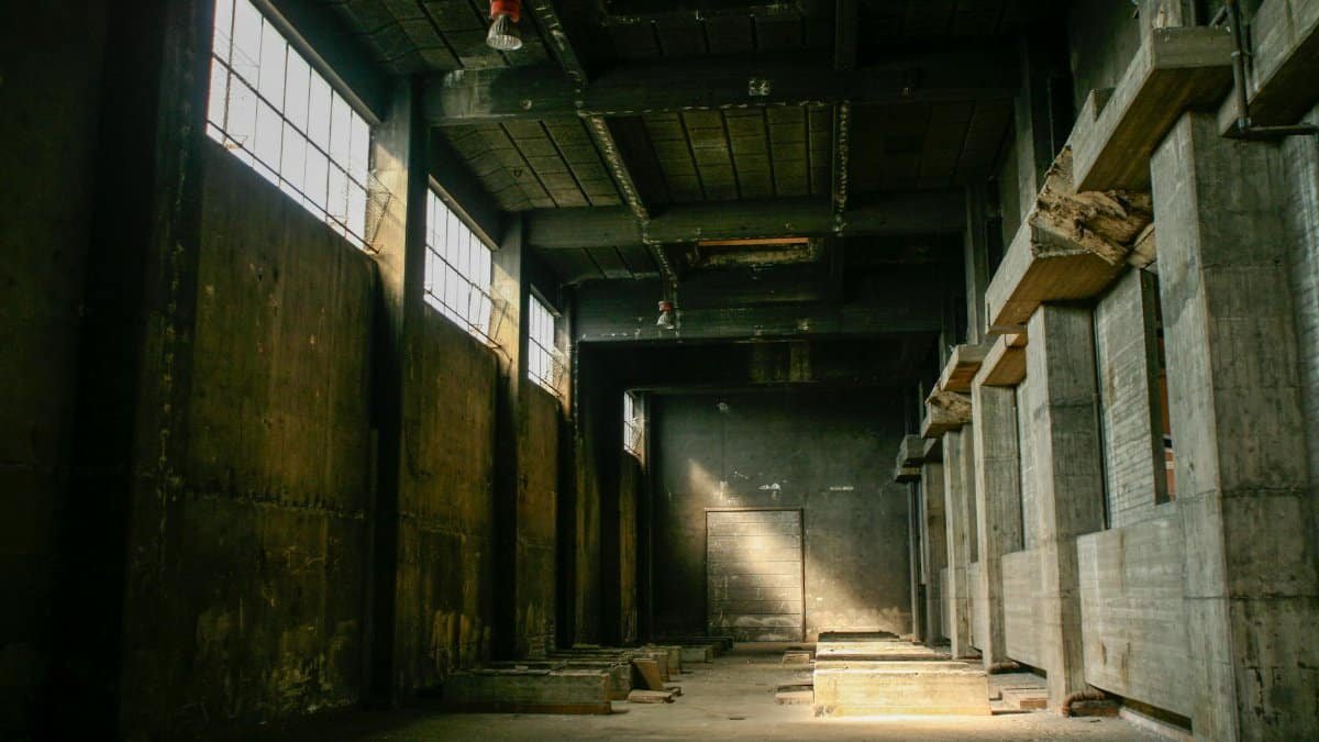 Explore an eerie, deserted industrial warehouse with dramatic lighting and shadows.