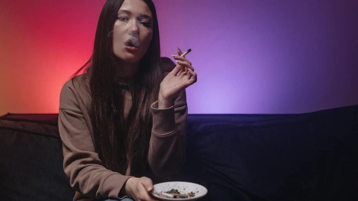 A woman smoking in a neon-lit room, seated on a couch, exuding calm vibes.