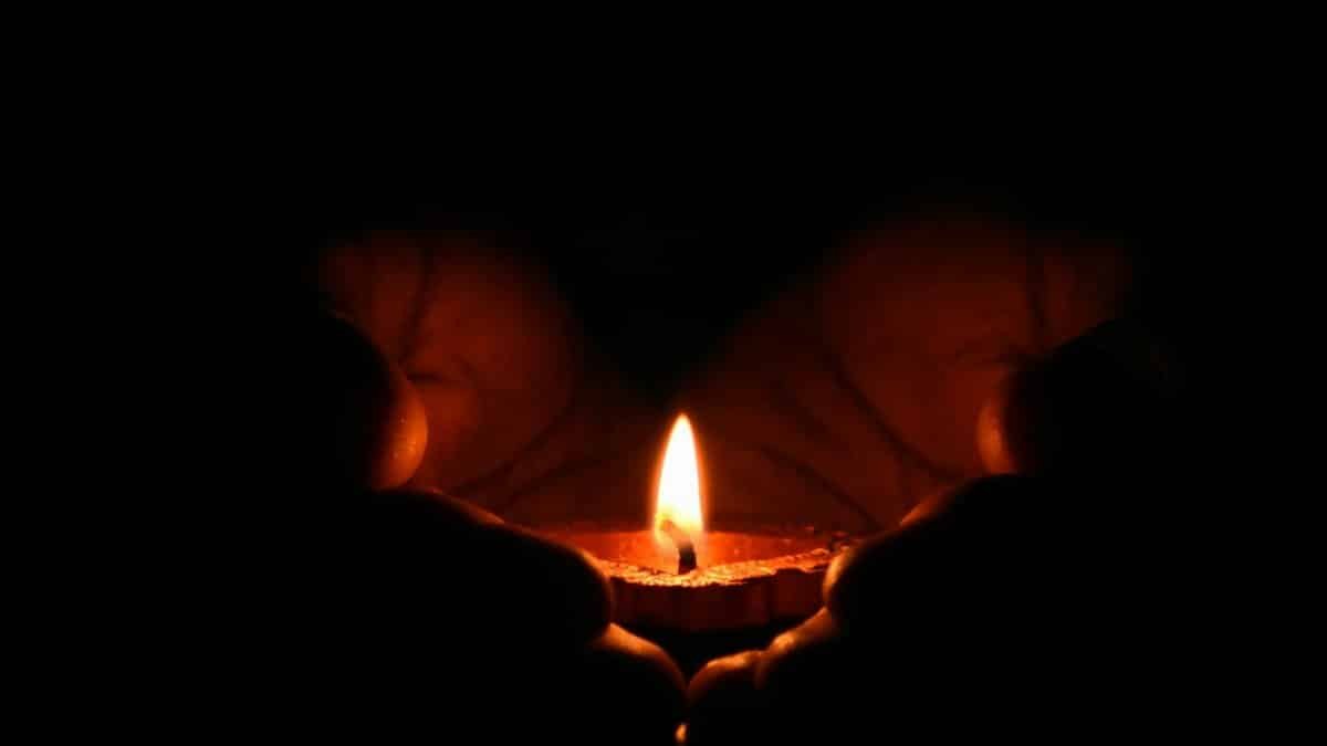 Close-up of hands warmly embracing a lit candle in the dark, creating a cozy atmosphere.