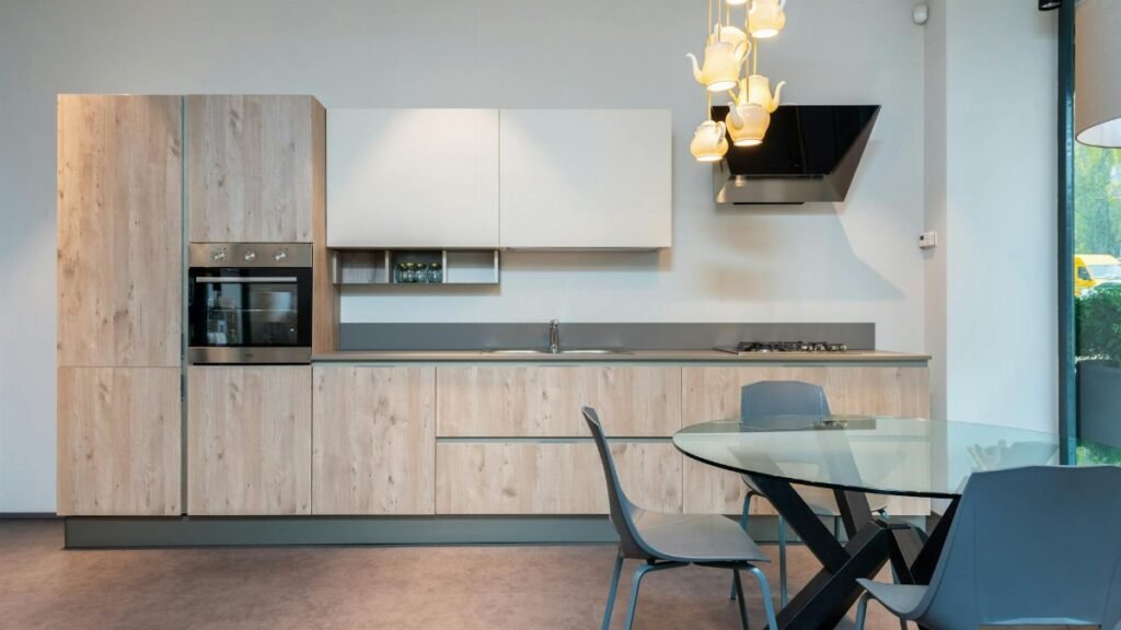 Stylish interior of spacious kitchen with light furniture and round glass dining table with chairs in modern apartment