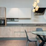 Stylish interior of spacious kitchen with light furniture and round glass dining table with chairs in modern apartment
