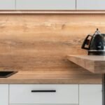 A sleek modern kitchen with wooden backsplash and black kettle, highlighting minimalist design.