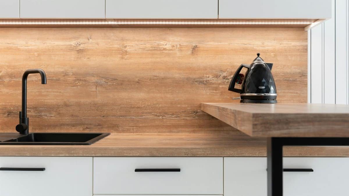 A sleek modern kitchen with wooden backsplash and black kettle, highlighting minimalist design.