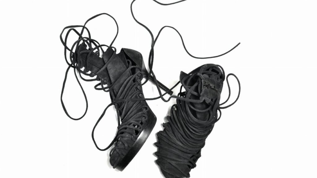 Pair of stylish black lace-up high-heeled boots on a white background showcasing intricate laces.