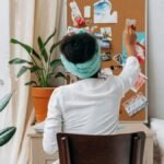 A woman in a cozy room organizing a vision board with photos and ideas.