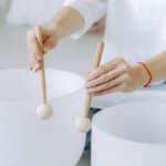 Hands playing crystal singing bowls with mallets, highlighting sound healing practice indoors.