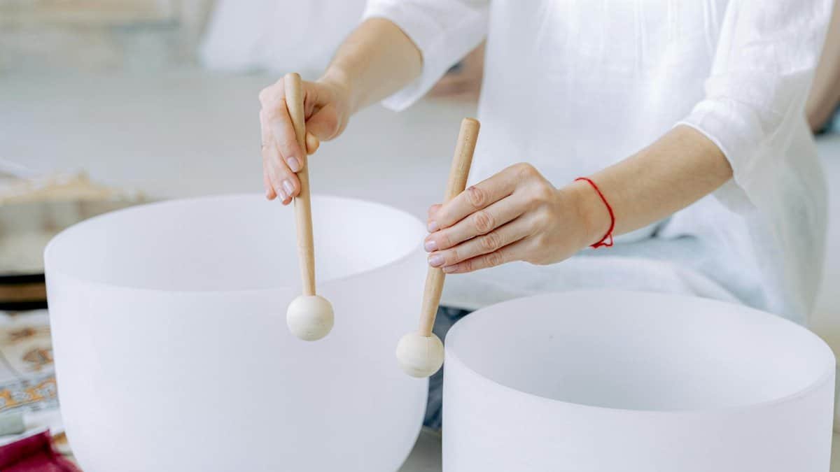 Hands playing crystal singing bowls with mallets, highlighting sound healing practice indoors.